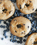 Overhead view of gluten-free blueberry bagels surrounded by fresh blueberries on a light surface