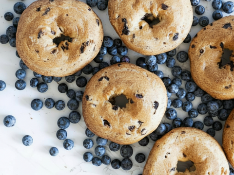 Overhead view of gluten-free blueberry bagels surrounded by fresh blueberries on a light surface
