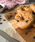 Gluten-free cinnamon raisin bagels from Outside The Breadbox on a wooden board with raisins and cinnamon