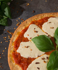 Top view of gluten-free margherita pizza topped with tomato sauce, melted mozzarella, fresh basil leaves, and red pepper flakes