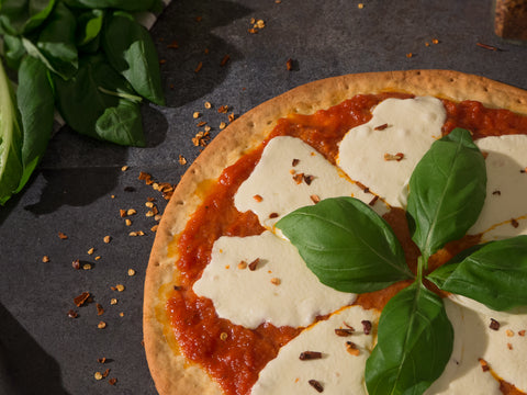 Top view of gluten-free margherita pizza topped with tomato sauce, melted mozzarella, fresh basil leaves, and red pepper flakes