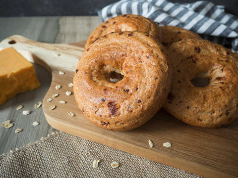 Gluten-free oat cheddar bagels from Outside The Breadbox on a wooden board with oats and cheddar