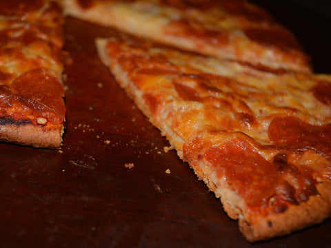 Close-up of a gluten-free pizza slice with melted cheese and pepperoni on a baked crust